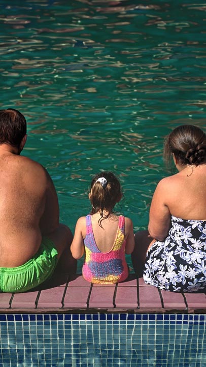Rückenansicht von zwei übergewichtigen Erwachsene an einem Pool mit einem normalgewichtigen Kind zwischen sich